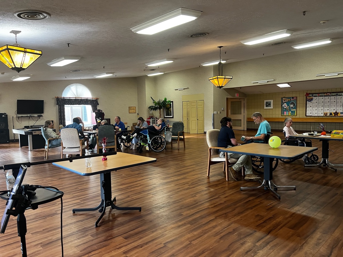 Residents gathered at tables in a care community activity room set up for a concert