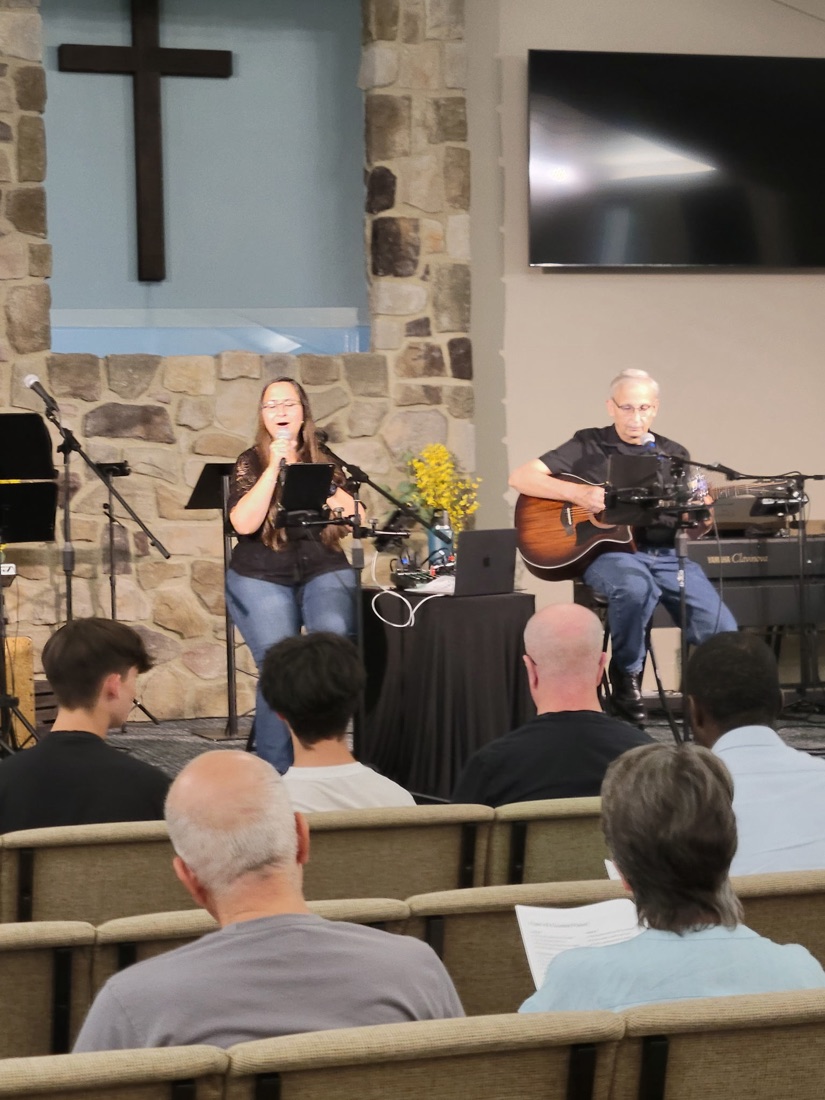 Jess singing and Keith on guitar beneath a wooden cross