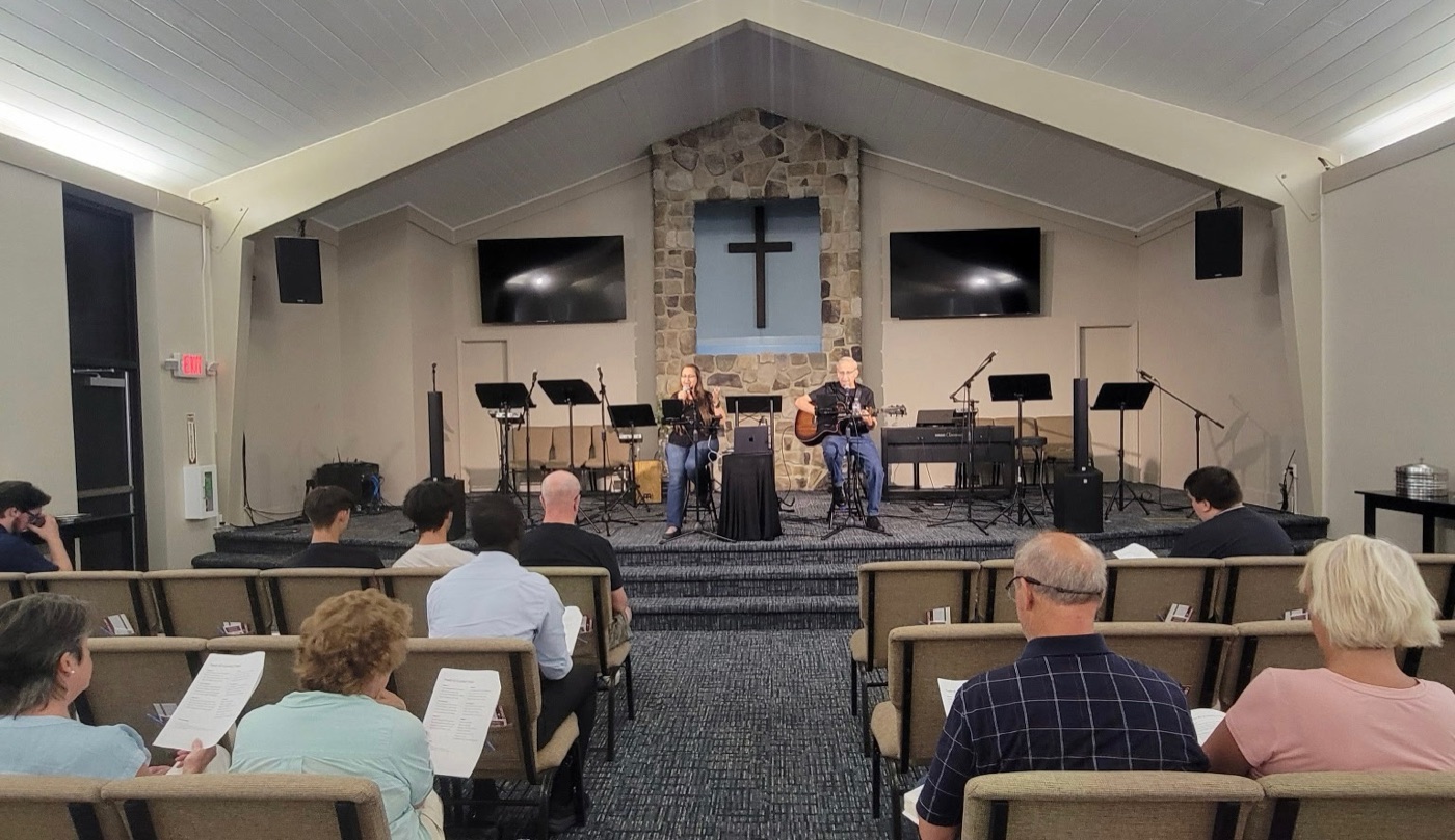 Jess and Keith leading a concert from the stage of a sanctuary with a stone cross