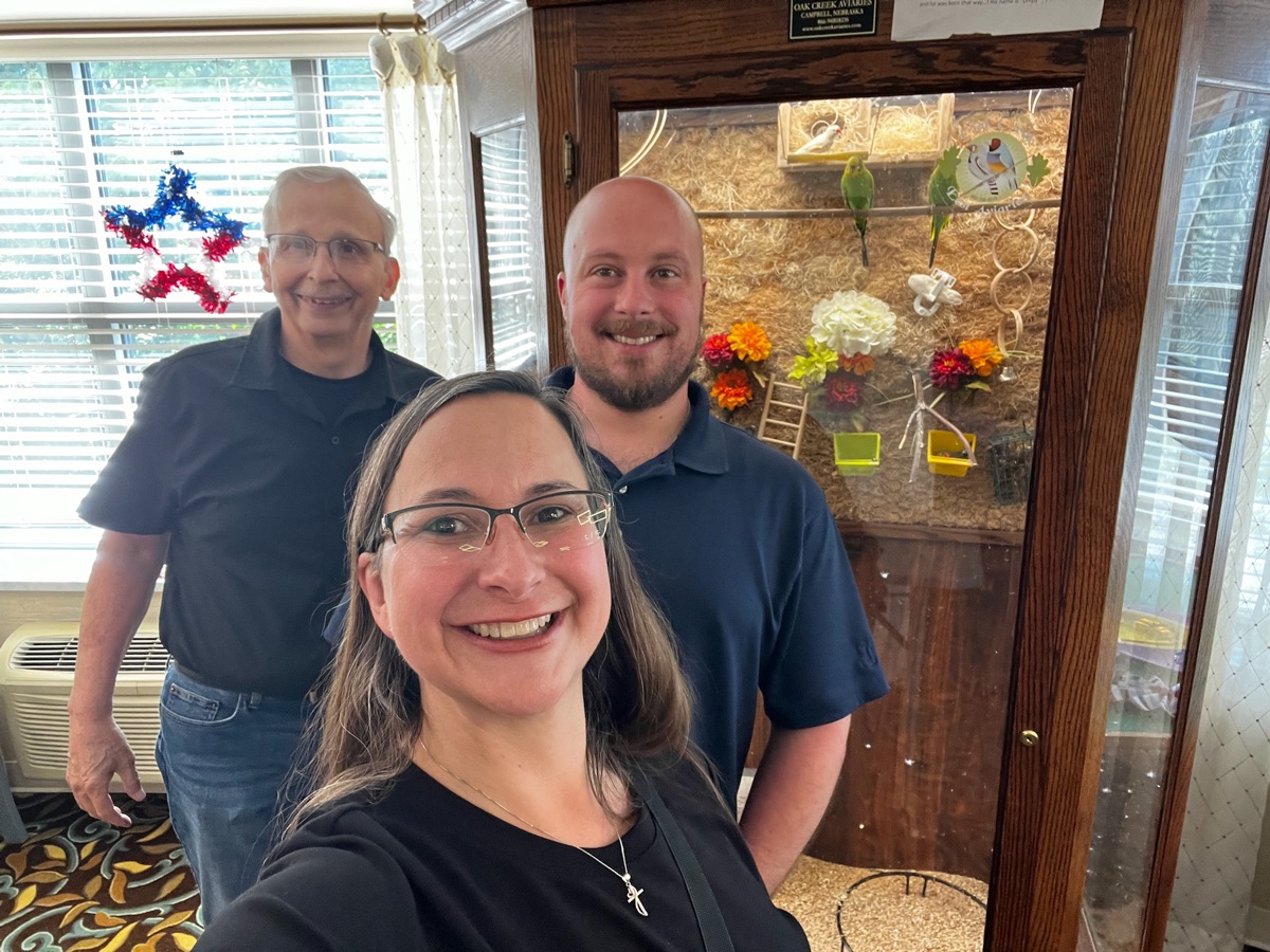 Three team members smiling beside a bird aviary
