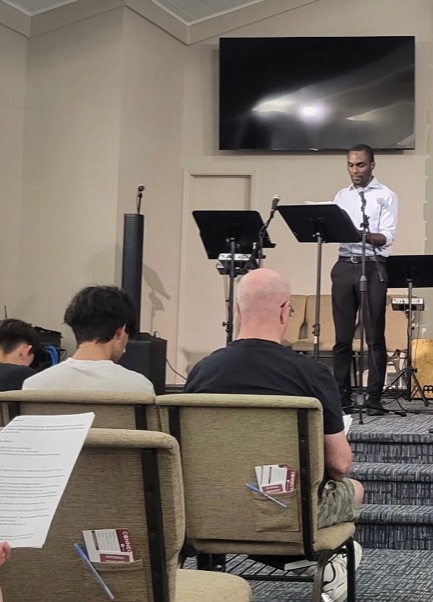 A team member reading a message from a music stand as people listen